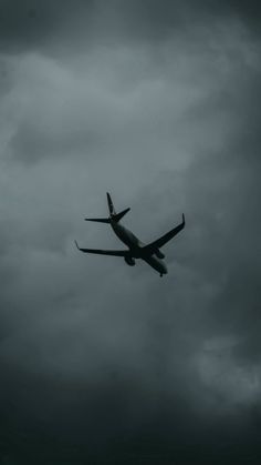 an airplane is flying in the sky on a cloudy day with dark clouds behind it