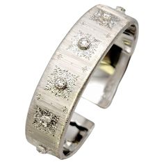 This exquisite, handcrafted bracelet by famed Italian jewelry designer, Mario Buccellati is absolutely stunning. It features seven sparkling natural round diamonds bezel set in 18 karat white gold. Surrounding each diamond is a finely detailed engraved design, adding to the elegant charm of this luxurious piece. The bracelet itself is done in a rigato finish, allowing the diamonds and engravings to really stand out against the stunning finish. The bracelet also has a hinged side, allowing for ea Luxury Designer White Gold Cuff Bracelet, Luxury White Gold Polished Cuff Bracelet, Luxury White Round Cuff Bracelet, Luxury Unique White Cuff Bracelet, Buccellati Bracelet, Italian Jewelry Designers, Buccellati Jewelry, Diamond Cuff Bracelet, Italian Jewelry