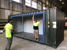 two men standing in front of a shipping container with their arms up and hands raised