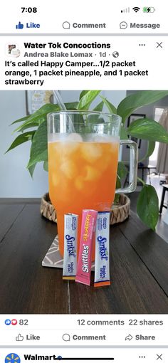 a glass filled with orange juice sitting on top of a table next to two packets of candy