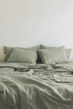 an unmade bed with green sheets and pillows on it in a white walled room