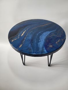 a blue coffee table with black legs and gold paint on the top, against a white background