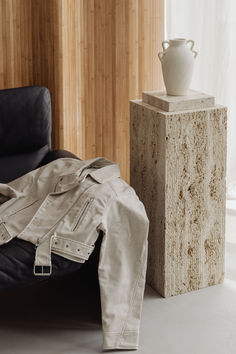 a white vase sitting on top of a table next to a black leather chair and ottoman