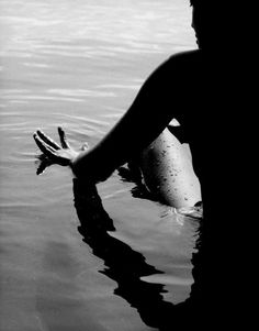 a person sitting in the water with their hand up to their face and legs crossed