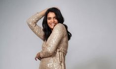 a woman in a gold sequin dress posing for the camera with her hands on her head