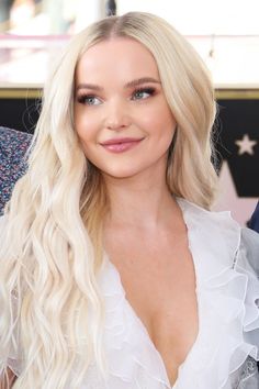 a woman with long blonde hair wearing a white dress and smiling at the camera while sitting down