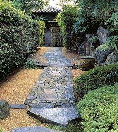 a stone path in the middle of a garden with trees and bushes around it, leading to an entrance