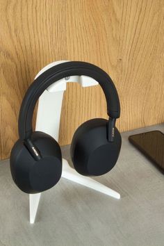 two black headphones sitting on top of a white stand next to a wooden wall