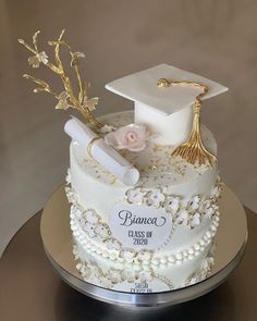 a white graduation cake with gold accents and flowers on top is adorned with a mortar, cap, and tassel