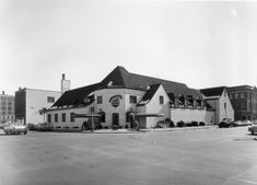 an old black and white photo of a large building with cars parked in front of it