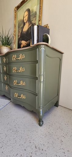 a green painted dresser with gold details and a painting on the wall in the background