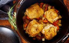 chicken and vegetables cooking in a skillet on a wooden table with utensils