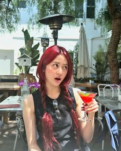 a woman with long red hair holding a drink in her hand and looking surprised at the camera