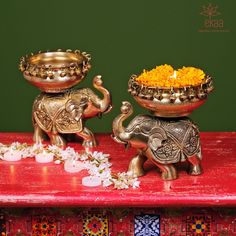 two brass elephants with flowers in their trunks on a red table next to each other