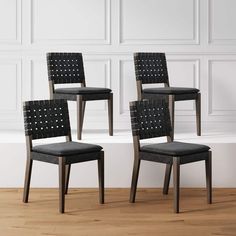 three black chairs sitting on top of a hard wood floor next to a white wall