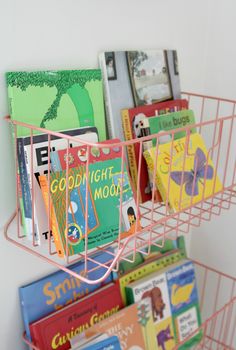 a pink basket filled with books sitting on top of a shelf next to a wall