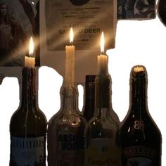 three bottles with candles in them are sitting next to two empty beer bottles and a clock