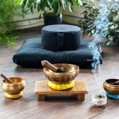 an assortment of brass bowls and incense sticks on a wooden table in front of a potted plant