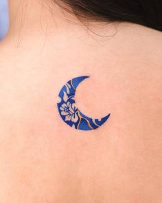 a woman's back with a blue and white flowered crescent tattoo on her left shoulder