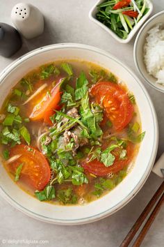 a white bowl filled with soup next to rice and chopsticks on a table