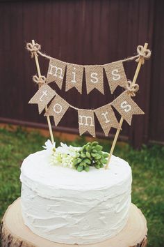 a white cake topped with a bunting banner and succulents sitting on top of a tree stump