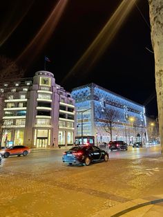 cars are parked on the street in front of tall buildings at night with bright lights