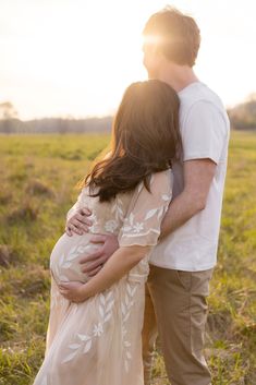 a pregnant couple cuddles while the sun shines through the grass behind them