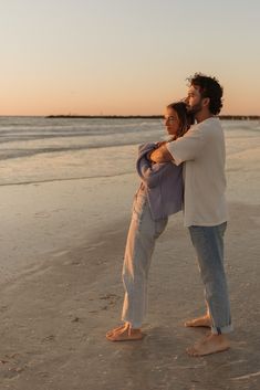 a man and woman are standing on the beach at sunset, one is holding his arm around the other's back