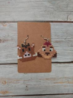 two cross stitch animal earrings sitting on top of a piece of brown paper next to each other