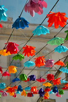 colorful paper umbrellas hanging from wires in front of a building with blue sky behind them