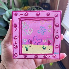 a hand holding up a small pink square with flowers and hearts painted on the inside