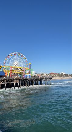 a ferris wheel sitting on top of a wooden pier next to the ocean in front of a blue sky