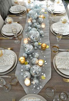 a long table is set with silver and gold christmas balls, candles, and plates