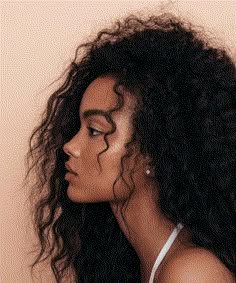 a woman with long curly hair wearing a white tank top looking off to the side