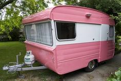 a pink and white trailer parked on the side of a road next to a tree