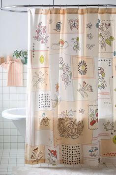 a shower curtain with pictures on it in a white tiled bathtub area next to a toilet and sink