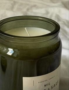 a green candle sitting on top of a white bed next to a black glass jar