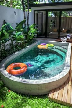 an inflatable pool surrounded by lush green plants and wooden decking with floating toys