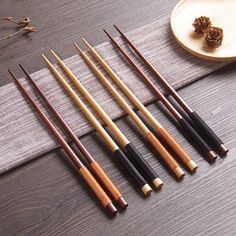 five pool cues lined up next to each other on a wooden table with pine cones in the background