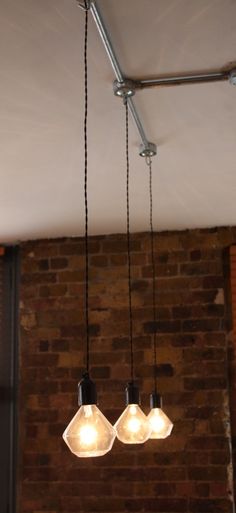 three light bulbs hanging from the ceiling in a room with brick walls and exposed ceilings