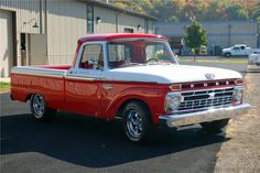 an old red and white truck parked in front of a building on a parking lot