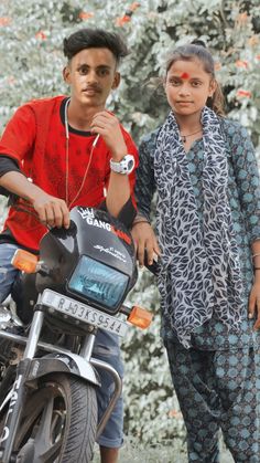 two people standing next to each other on a motorcycle