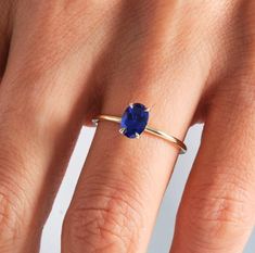 a woman's hand with a blue ring on top of her finger and an oval shaped sapphire stone in the middle