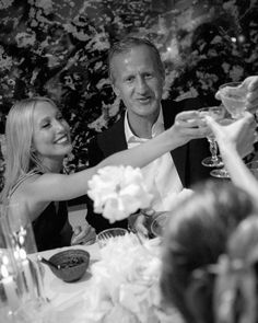 black and white photograph of two people toasting at a table with flowers on it