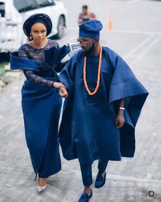 two people dressed in blue walking down the street with one woman wearing an orange beaded necklace