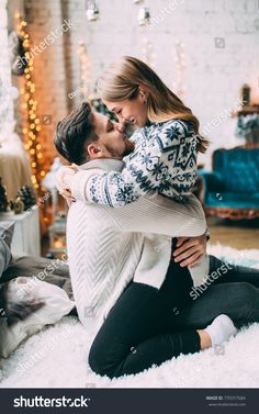 a man and woman are kissing on the floor in front of christmas tree, with lights behind them