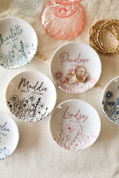 six personalized wedding rings are placed in small bowls on a white tablecloth with floral designs