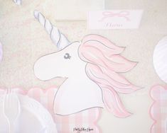 a pink and white unicorn themed table setting with paper plates, napkins and place cards