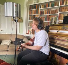 a young man sitting in front of a piano with headphones on playing the guitar