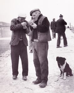 two men standing next to each other with a dog looking at something in their hands